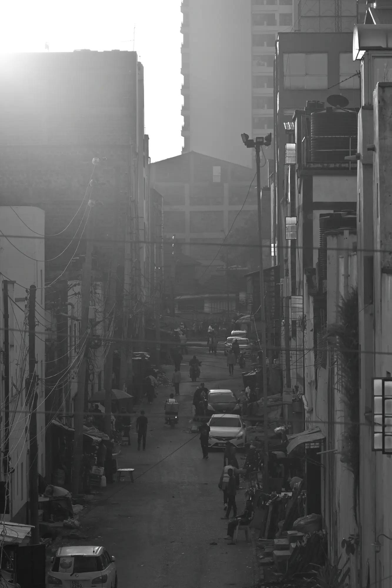 Low sun flares down a hazy Nairobi side street, traders and matatus layered into silver depth