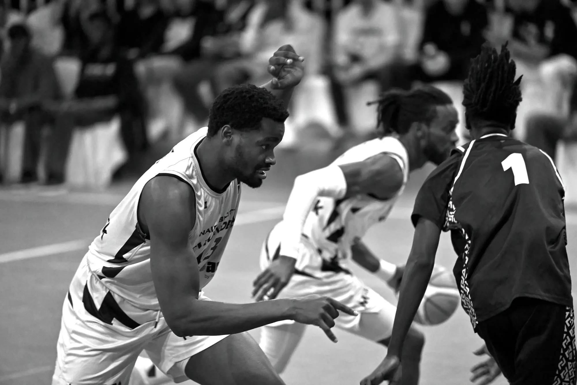 Nairobi City Thunder player crouched low, fist up and pointing, as a teammate drives at a dark-shirted defender