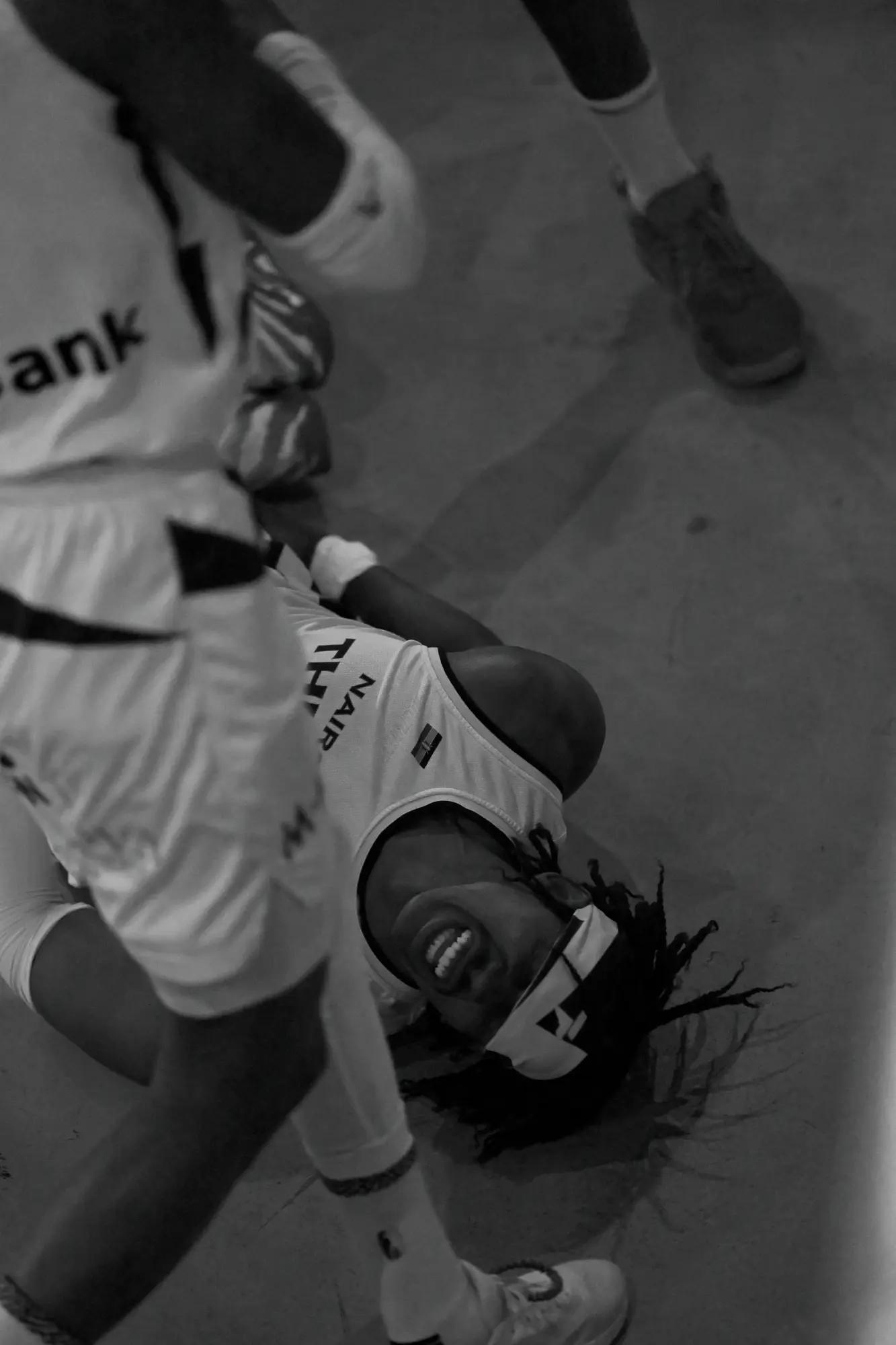 Nairobi City Thunder player sprawled on the court mid-grimace as play surges past overhead