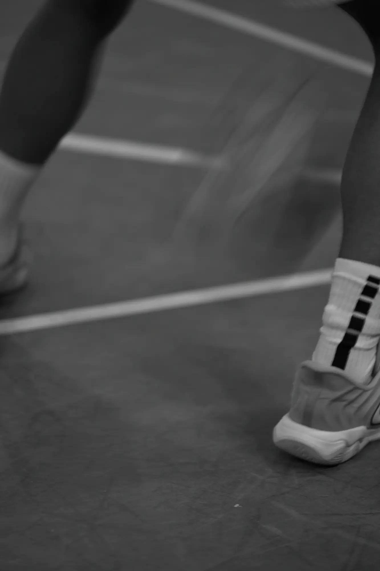 A planted shoe and taped sock sharp against blurred court lines, another foot lifting away