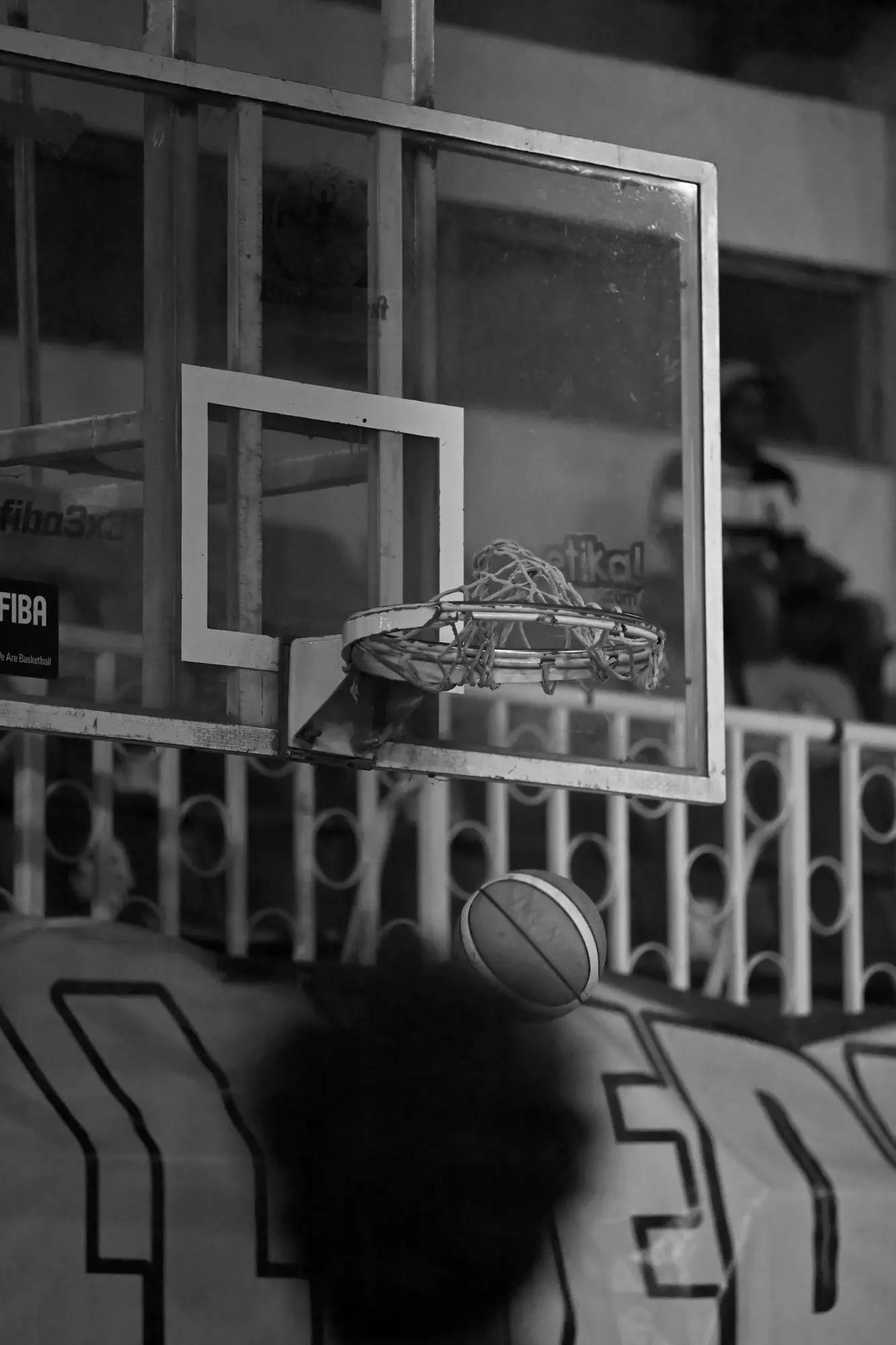 Backboard, rim and tangled net stacked above a ball in flight and the repeating circles of a barrier