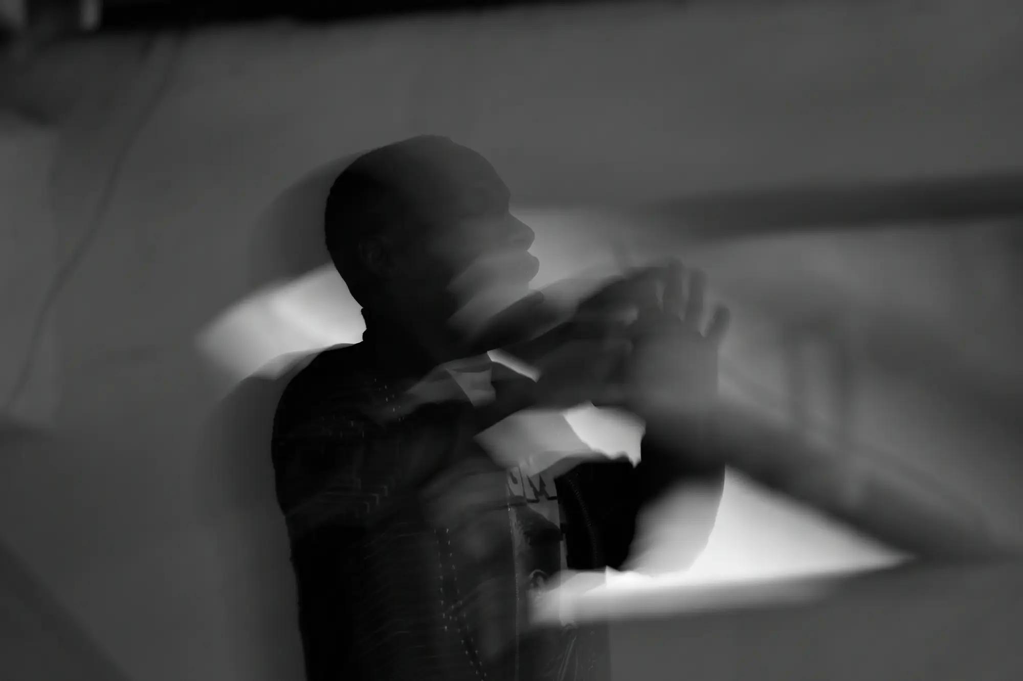 A player in a dark warm-up top clasps his hands at his face, doubled against a pale lit wall