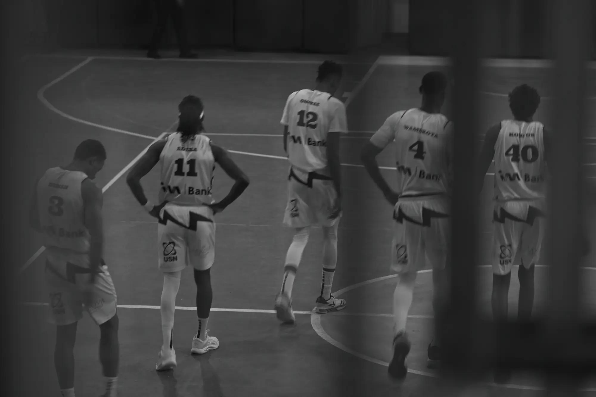 Five Thunder players in white walk back up the court, seen past a dark pillar and softened by a slow shutter